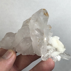 Pode incluir: Um aglomerado de cristais de quartzo transparentes com algumas pequenas inclusões douradas. Os cristais estão dispostos em uma formação pontiaguda e irregular.