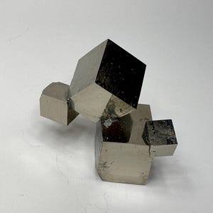 以下が含まれることがあります： 鋭く明確な立方体の形状をした金属質の黄鉄鉱の結晶クラスター。この鉱物標本は、反射性のある真鍮のような金色の表面を持ち、滑らかで平らな面と幾何学的なエッジが特徴で、自然に連結した結晶構造を示しています。