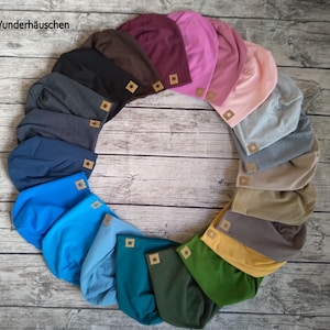 Könnte beinhalten: Eine Sammlung von 15 bunten Strickmützen mit einem sternförmigen Logo. Die Mützen sind in einem Kreis auf einer Holzoberfläche angeordnet.
