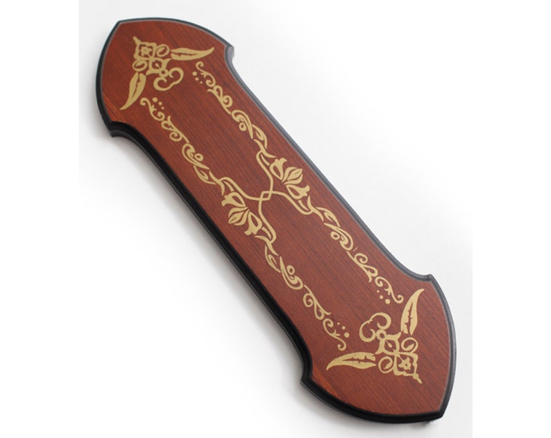 May include: A wooden sword display plaque with a dark brown finish and gold floral designs. The plaque has a pointed top and bottom.