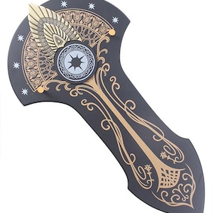 May include: A black decorative shield with gold and white detailing. The shield has elaborate gold patterns, including a central emblem and star motifs. A gold wing-like element is at the top.