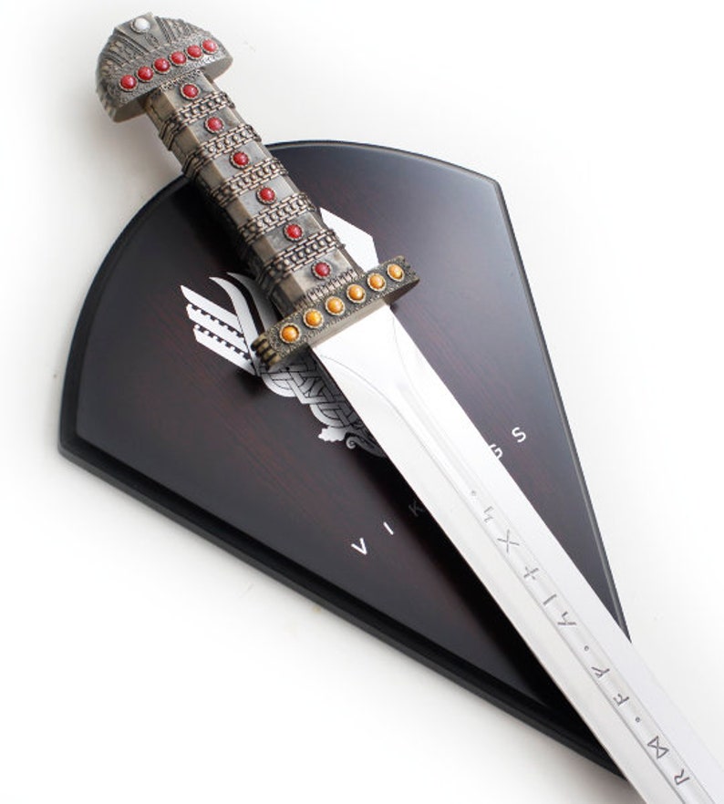 May include: A silver Viking sword with a red and gold hilt mounted on a dark wood shield with a Viking symbol and the word "VIKING" inscribed on it.