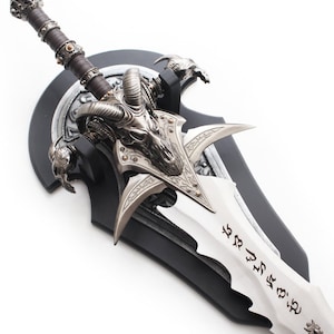 May include: A decorative fantasy sword with a silver blade and intricate metalwork. The hilt is wrapped in brown leather, and the guard features a skull design. The sword is mounted on a black plaque.