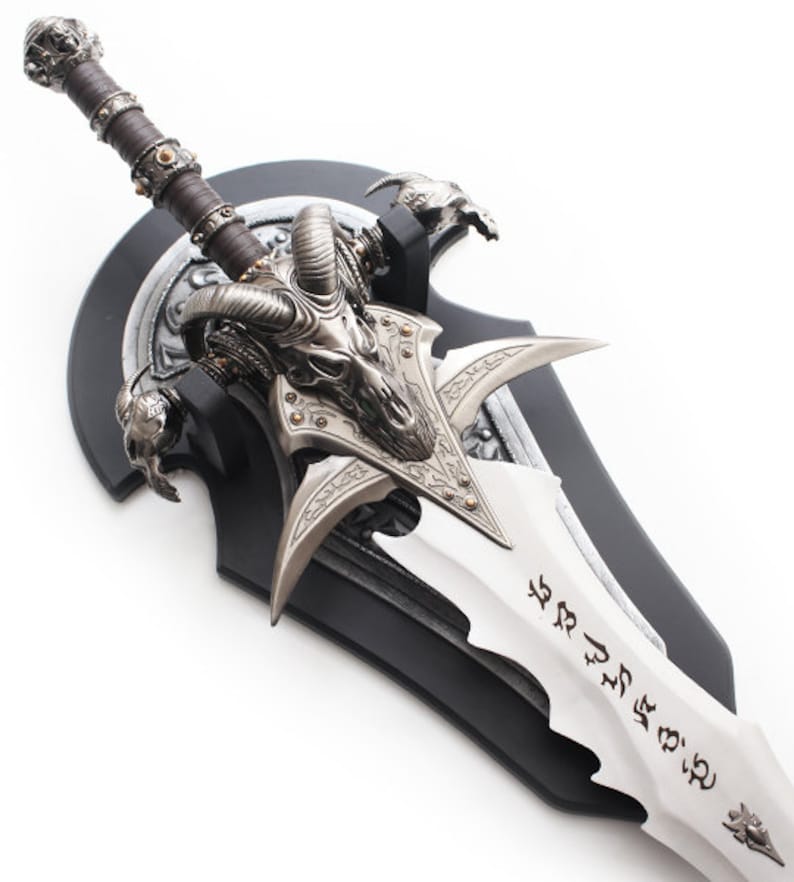 May include: A decorative fantasy sword with a silver blade and intricate metalwork. The hilt is wrapped in brown leather, and the guard features a skull design. The sword is mounted on a black plaque.