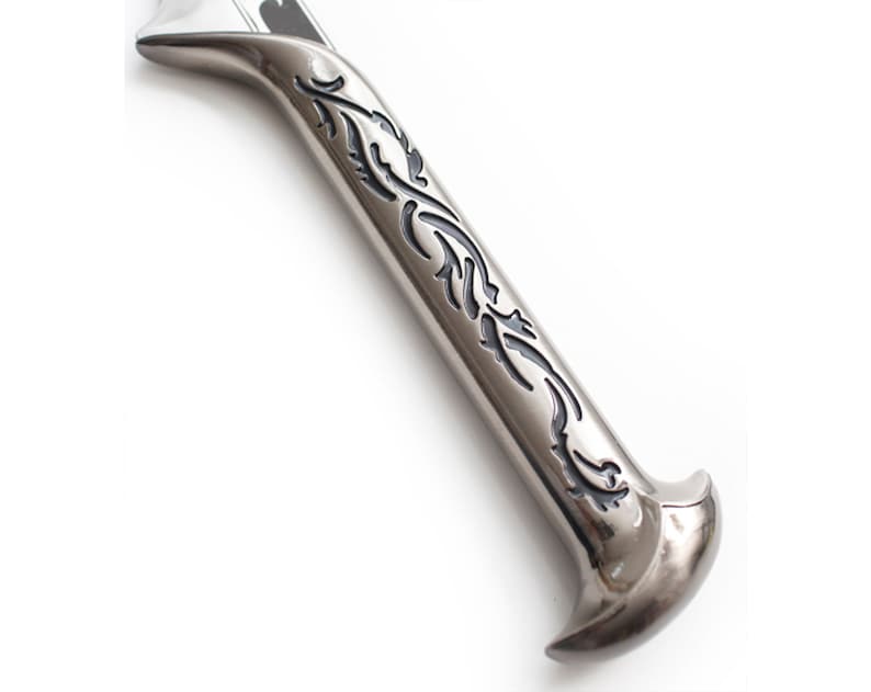 May include: Close-up of a silver sword hilt with a black floral design.