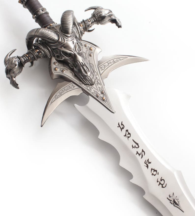 May include: A detailed, silver-colored fantasy sword with a skull-shaped hilt and curved horns. The blade has a series of notches and etched symbols. The hilt features intricate detailing and a leather-wrapped grip.