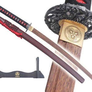 Może przedstawiać: Japoński miecz katana z drewnianą rękojeścią i ostrzem. Rękojeść jest owinięta czarną i czerwoną tkaniną. Pochwa jest brązowa z czerwonymi akcentami. W zestawie czarny drewniany stojak ze złotym emblematem.