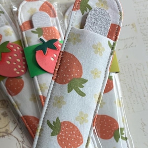 May include: Four white nail file holders with a strawberry pattern. The holders are made of fabric and have a clear plastic sleeve. Each holder has a gray nail file inside.