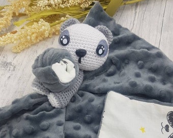 May include: A gray and white crocheted panda plush toy attached to a gray and white baby blanket with a white side featuring a black and white panda print with yellow stars and a yellow crown.
