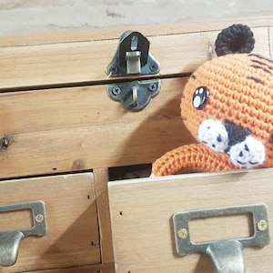 May include: A crocheted orange tiger stuffed animal with black stripes and white accents peeks out of a wooden drawer with a label that reads "E de la Facture".
