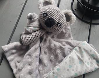 May include: A gray crocheted koala stuffed animal with black eyes and a black nose is attached to a gray and white polka dot blanket. The blanket has a white side with gray polka dots and a white side with blue and yellow polka dots.