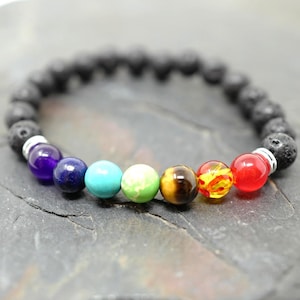 Op de afbeelding: Een zwarte lavastenen armband met zeven chakra-parels. De parels zijn paars, blauw, turquoise, groen, bruin, geel en rood.