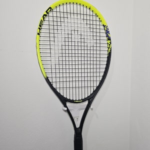 May include: A black and yellow tennis racket with the word "HEAD" printed on the frame. The racket is hanging on a white wall.