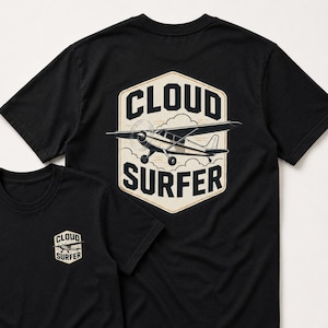 May include: Black t-shirts with a graphic of a small airplane inside a cream-colored hexagon. The text "CLOUD SURFER" is above and below the plane. A smaller version of the design is on the front of one shirt.