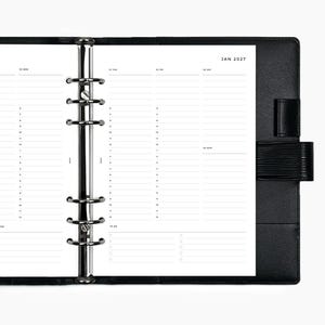 May include: An open black leather binder featuring a six-ring metal mechanism and white planner pages. The pages display a weekly schedule for January 2027 with hourly slots, a to-do list section, and printed text including JAN 2027.