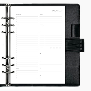 May include: A black leather bound daily planner with a silver ring binder. The planner has sections for priorities, to do, schedule, meals, and habits. The planner has a black leather flap with a silver clasp.