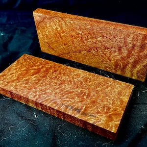 May include: Two pieces of wood with a reddish-brown colour and a swirling grain pattern. The wood is likely for crafting or woodworking projects.