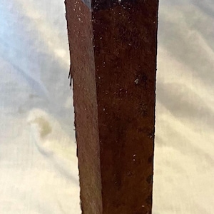 May include: A rectangular, dark brown wooden object with a slightly tapered shape. The top is a darker shade, and the sides show a rough, textured surface. The object appears to be a piece of wood, possibly for a craft project.