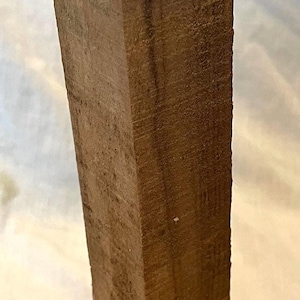 May include: A solid, rectangular wooden furniture leg, showcasing a rich, dark brown color with visible wood grain. The top edge has a rough, unfinished texture, while the sides are smooth. This leg is designed for furniture.