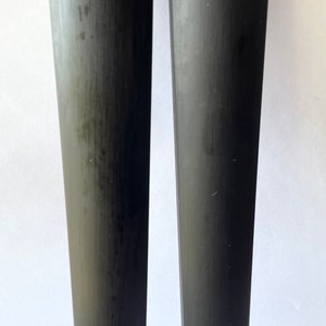 May include: Two black violin shoulder rests. The rests are made of a smooth, dark material and have a slightly curved shape.