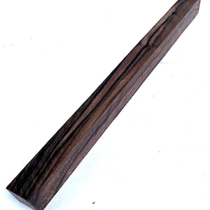 May include: A rectangular block of dark brown wood with black grain patterns. The wood has a smooth, polished appearance and is cut at an angle on one end. The wood is likely used for woodworking projects.