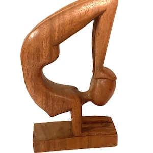 Peut inclure: Sculpture en bois représentant une personne en position de yoga. La figurine est sculptée dans un bois brun clair et est positionnée dans une posture gracieuse et arquée. La sculpture est montée sur une base rectangulaire.