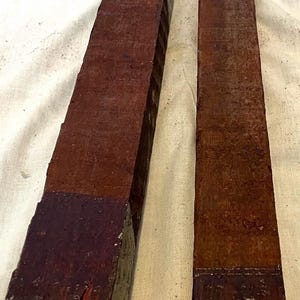 May include: Two rectangular wooden blocks with a dark reddish-brown color. The blocks have a rough, textured surface and are painted with a darker shade of reddish-brown at the ends. The blocks are of different sizes.
