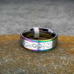 May include: A silver ring with a rainbow colored band and the word "Woof" engraved on it, with a heart on either side of the word.