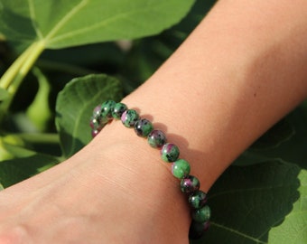 May include: A green and pink gemstone bracelet with round beads. The bracelet is worn on a person's wrist.