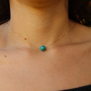 May include: A delicate gold chain necklace with a single round turquoise gemstone pendant.