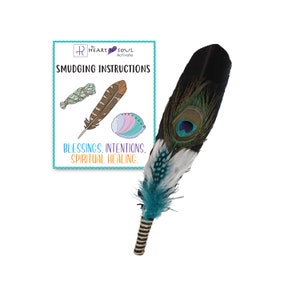 May include: A peacock feather smudging fan with turquoise and white feathers. The fan is tied with a black and white striped ribbon. A card with the text "Heart & Soul Activate" and "Smudging Instructions" is in the background. The card also includes the text "Blessings. Intentions. Spiritual Healing."