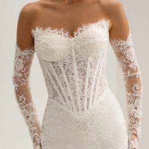 May include: A white strapless corset bodice dress featuring intricate floral lace detailing, a sweetheart neckline with scalloped edges, and matching long, sheer lace sleeves that extend to the wrists, creating a cohesive and detailed appearance.
