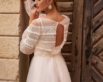 Könnte beinhalten: Ein weißes, bodenlanges Kleid mit langen, transparenten Ärmeln aus Spitze, einem taillierten Oberteil mit geometrischem Spitzenbesatz, einem offenen Rückenausschnitt mit einem Knopf am Halsausschnitt und einem fließenden Tüllrock.