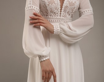 May include: A floor-length white dress featuring a deep V-neckline with intricate lace detailing on the bodice. The garment has long, sheer bishop sleeves with lace inserts at the shoulders and cuffs, and a flowing skirt made of lightweight fabric.