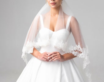 May include: A bride wearing a white wedding dress with a lace trim and a veil. She is wearing a tiara and has her hair pulled back.