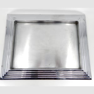 May include: A silver tray with a raised, decorative border. The tray has a rectangular shape and a smooth, reflective surface.