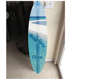 May include: A blue and white surfboard with the text "Locals Only" and "Chase" printed on it. The surfboard is leaning against a wall.