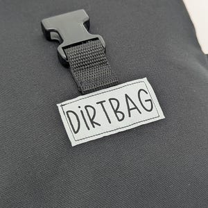 May include: A black canvas bag with a black buckle and a white label that says "DIRTBAG".