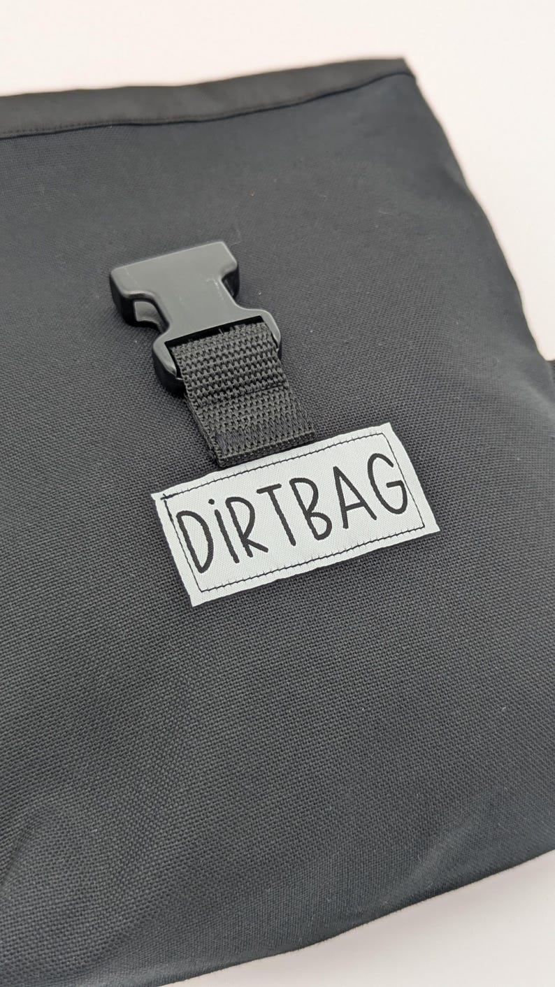 May include: A black canvas bag with a black buckle and a white label that says "DIRTBAG".