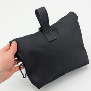 May include: Black canvas bag with a black strap and a silver carabiner clip.