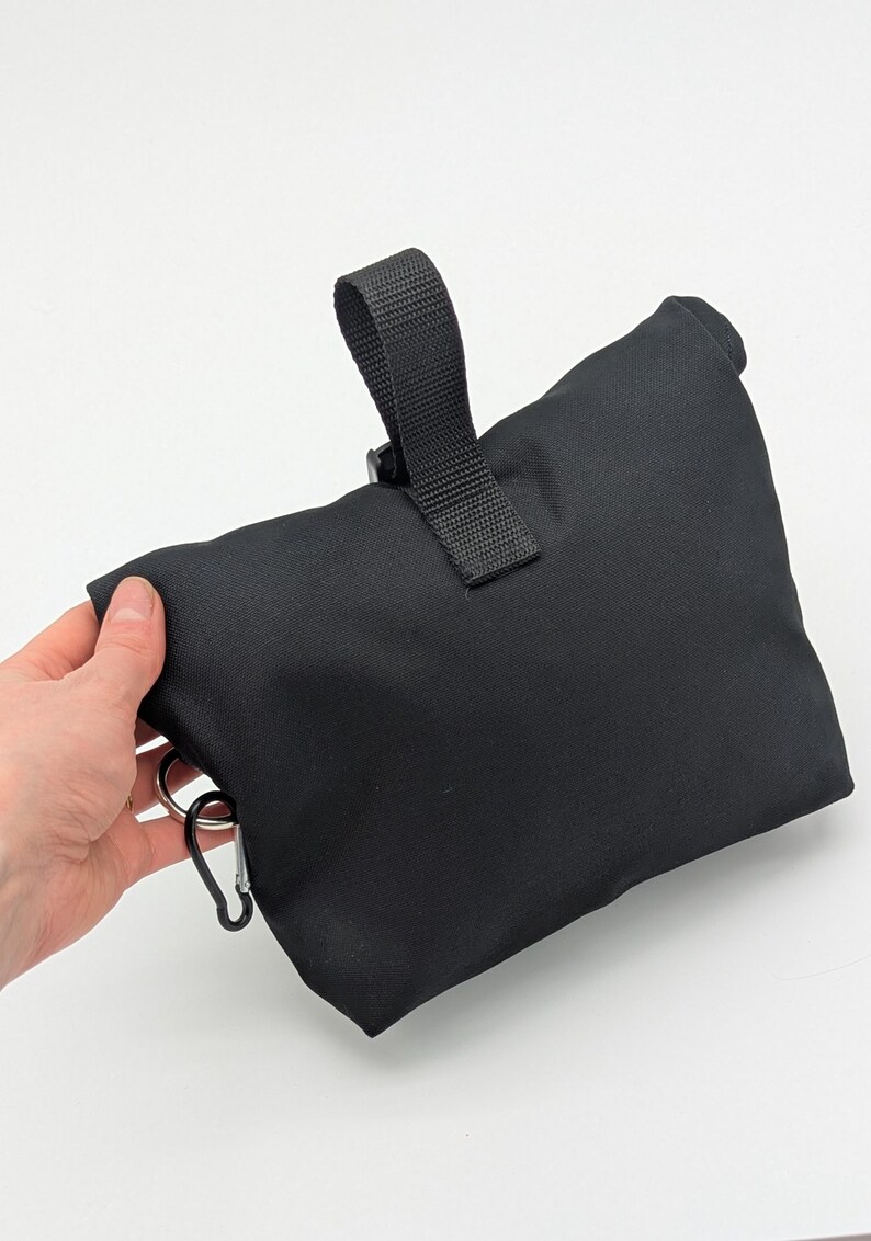 May include: Black canvas bag with a black strap and a silver carabiner clip.