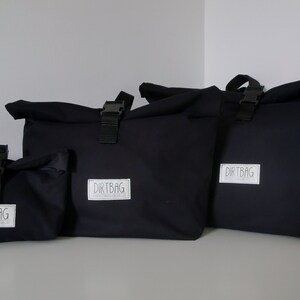 May include: Four black canvas bags with roll-top closures and adjustable straps. The bags have a white logo that reads "DIRTBAG" on the front.