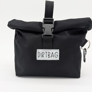 May include: Black canvas roll-top bag with a black buckle closure and a white label that says "DIRTBAG".