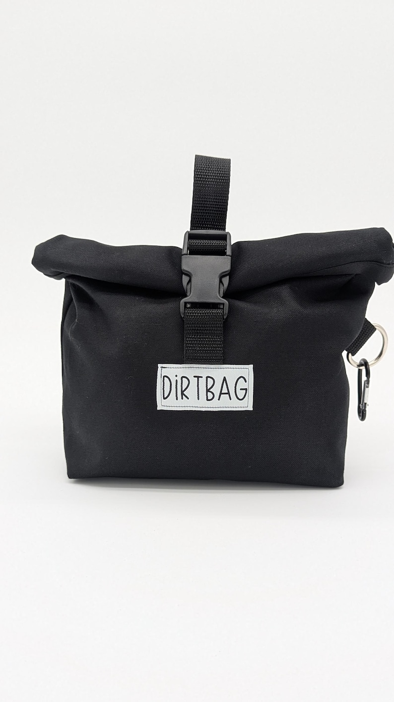 May include: Black canvas roll-top bag with a black buckle closure and a white label that says "DIRTBAG".