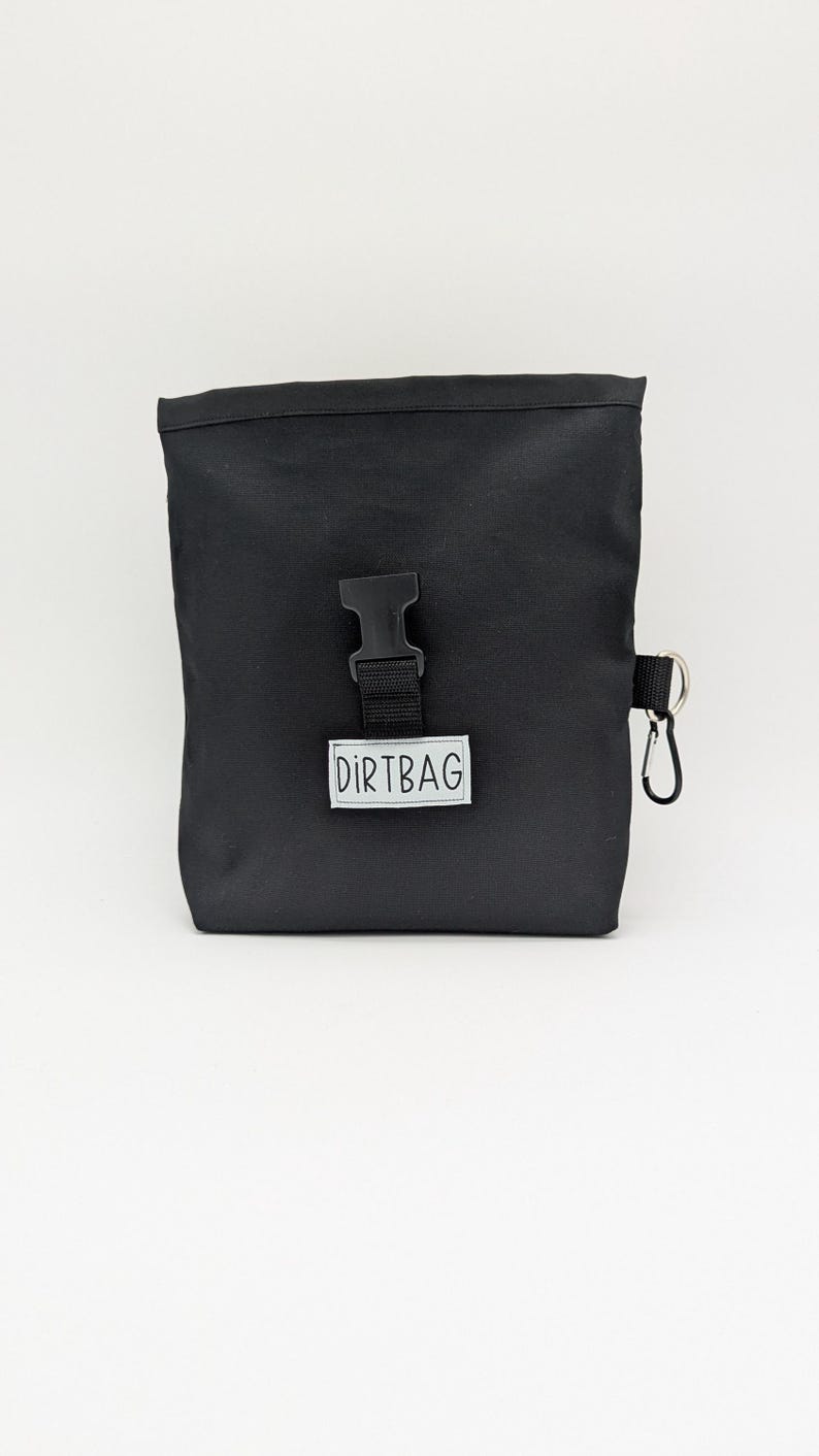 May include: A black canvas bag with a black buckle and a silver clip. The bag has a white label that says "DIRTBAG".