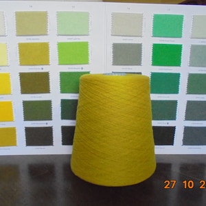 Puede incluir: Una bobina de hilo amarillo se muestra frente a una carta de colores con muestras de tela. La carta muestra una variedad de colores, incluyendo blanco, verde, marrón y amarillo. La fecha 27 10 2023 está escrita en la mesa debajo de la bobina de hilo.