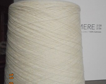 Puede incluir: Un cono de hilo blanco roto con el texto "CARIAGGI" y "MERE 2/28 2/36 n. 2/36 / 100% Cashmere" en una etiqueta blanca.