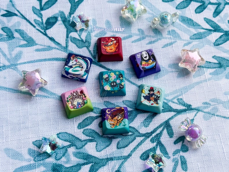 Puede incluir: Una colecci&oacute;n de siete teclas cuadradas para teclado mec&aacute;nico con coloridas ilustraciones inspiradas en el anime, que incluyen personajes como un duende del polvo, un gato-bus y un esp&iacute;ritu, acompa&ntilde;adas de varias cuentas transl&uacute;cidas con forma de estrella.