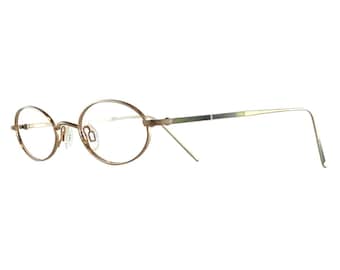 May include: Oval-shaped eyeglasses with a thin, gold-colored metal frame. The lenses are clear, and the temples are a thin, silver-colored metal. The glasses have a classic, minimalist design.