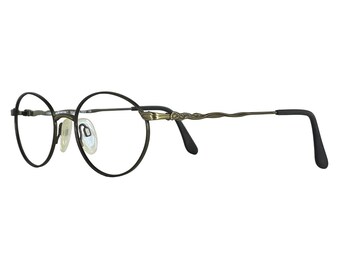 Peut inclure: Lunettes de forme ovale avec une monture noire et des branches décoratives de couleur bronze. Les verres transparents sont maintenus par une fine monture. Les branches sont légèrement incurvées et se terminent par des manchons noirs.